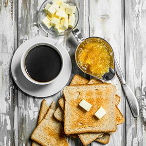 Pan tostado con mantequilla, mermelada y café caliente. Sobre fondo rústico de madera.
