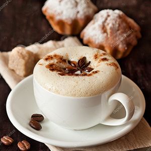 Primer plano de un café con leche con espuma y al fondo unas magdalenas.